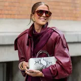 Kobieta w bordowej ramonesce i okularach przeciwsłonecznych prezentuje modne stylizacje na wiosnę, trzymając w ręku torebkę w wężowy wzór.