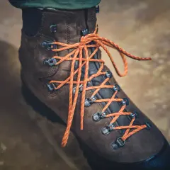 Brązowy but trekkingowy z pomarańczowymi sznurówkami, pokazujący, jak wiązać buty trekkingowe.