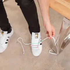 Instrukcja jak wiązać sneakersy: białe buty Adidas z czarnymi paskami, osoba zawiązuje sznurówki.