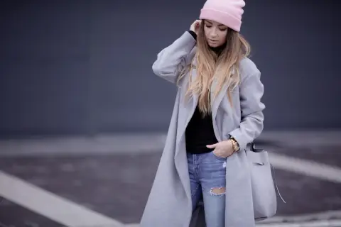 Modna dziewczyna w różowej czapce i szarym płaszczu, z podartymi jeansami. Stylowe stylizacje z szarym płaszczem na co dzień.