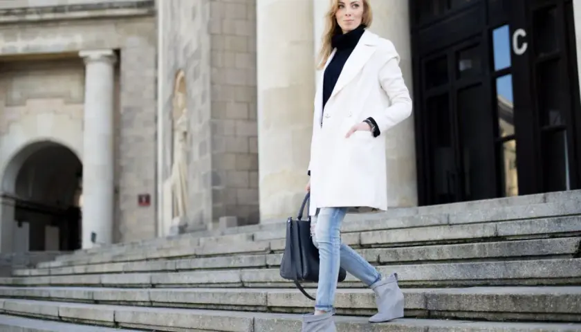 Elegancka kobieta w białym płaszczu i jeansach schodzi po schodach. Stylowe biały płaszcz stylizacje na co dzień.