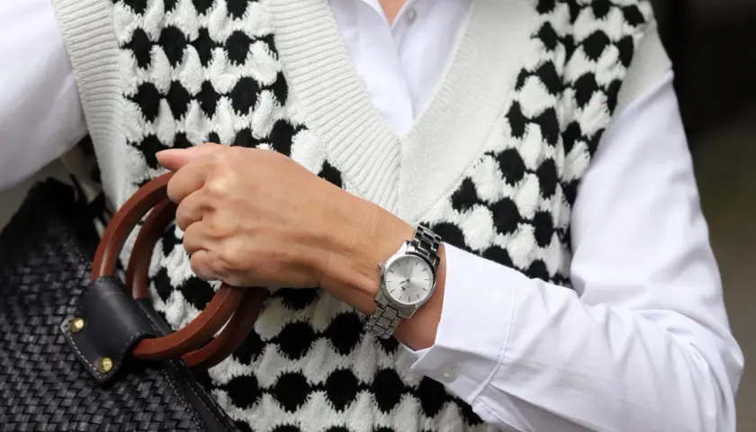 Elegancki zegarek na sztywnej bransolecie, dopełniający stylizację z białą koszulą i kamizelką w czarno-białe wzory.