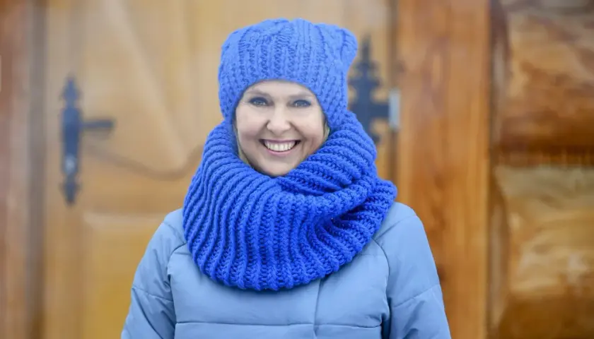 Uśmiechnięta kobieta w niebieskiej czapce i szaliku, idealny przykład, jak dobrać czapkę do płaszcza.